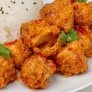 Close-up of spicy crispy chicken paired with jasmine rice garnished with sesame seeds and cilantro.