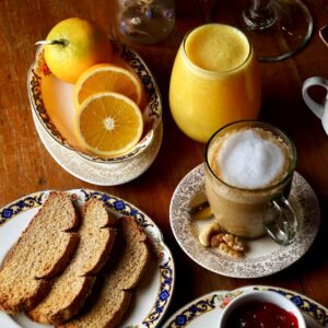 A cozy breakfast setup featuring bread, coffee, orange juices and garnishes on a wooden table.